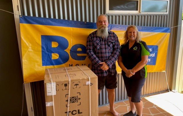 man with a woman in front of a social housing complex with a donated new dishwasher in an unopened box